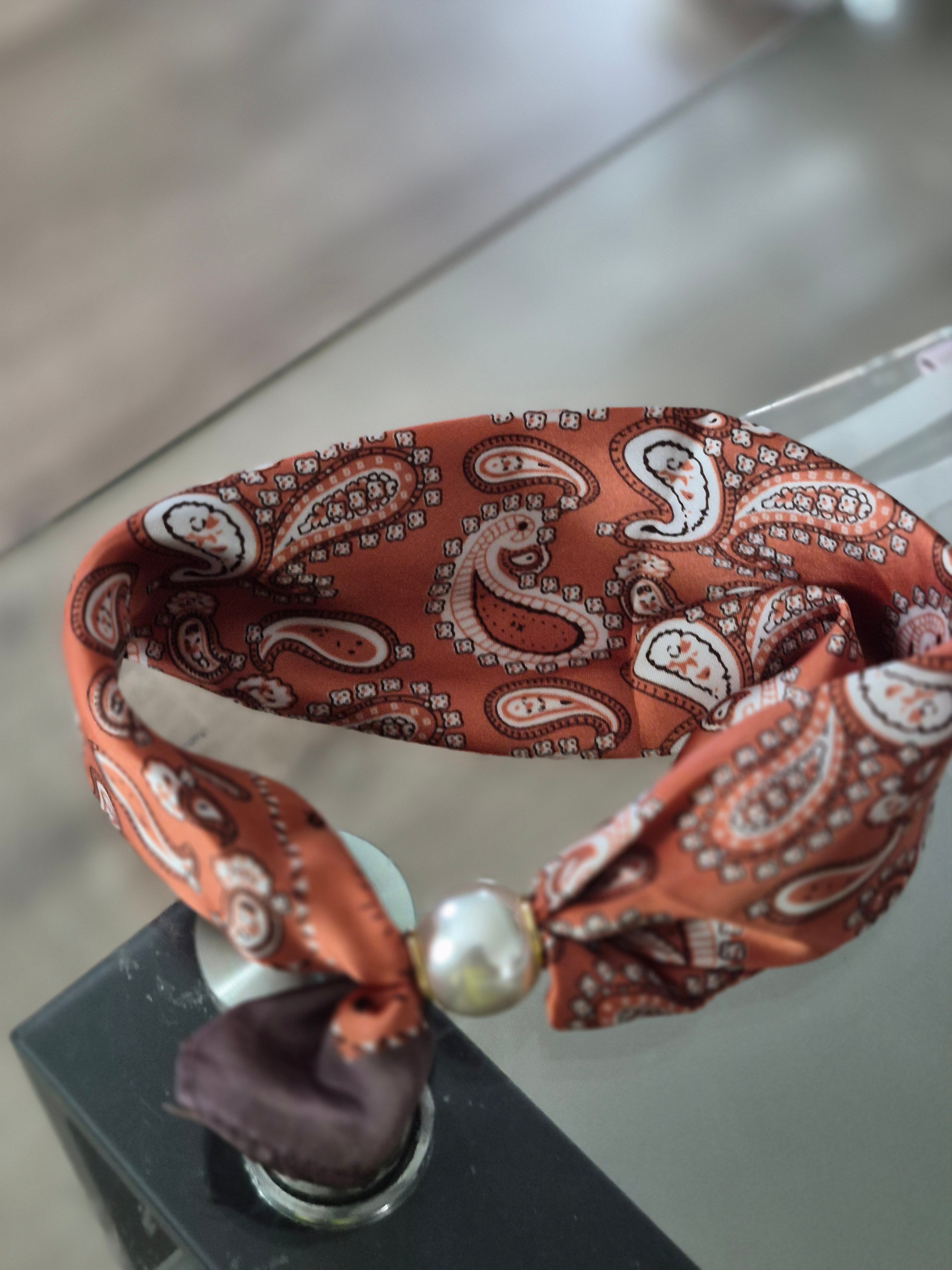Aria Floral Silk-Feeling Neckerchief Scarf with a Pearl Slide on a glass table, showcasing paisley design.